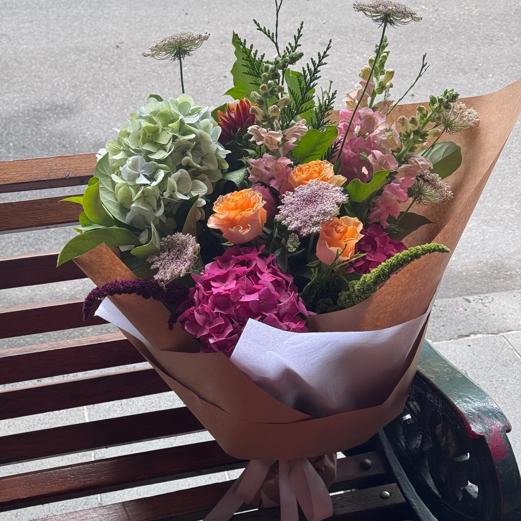 Bright coloured seasonal flowers paired with green foliage wrapped in beautiful paper finished with cream ribbon. 